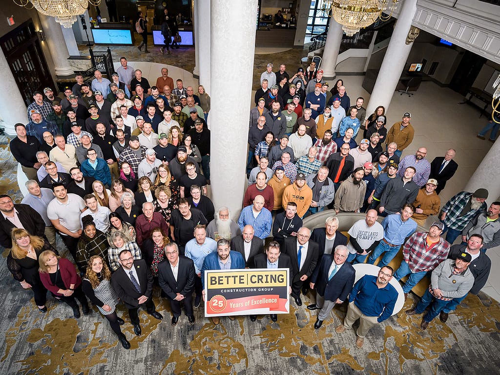 Bette & Cring employees gathered and smiling, while holding a "25 Years of Excellence" sign in a hotel lobby.