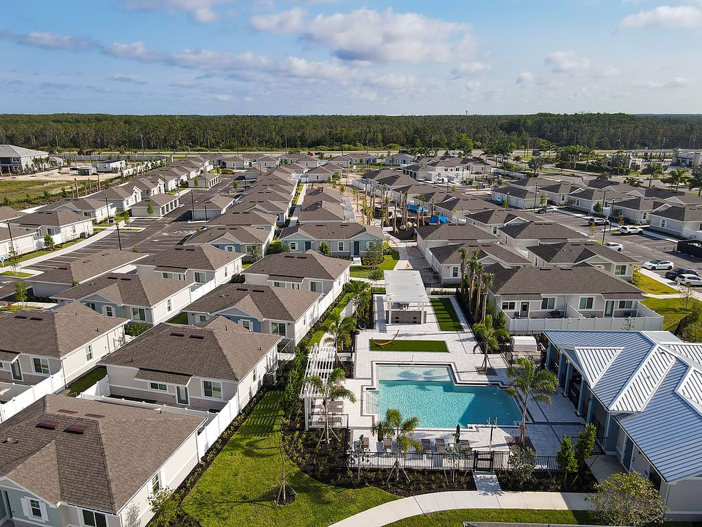 A housing community with one-story homes, fenced-in yards, a pool, a BBQ area and palm trees.