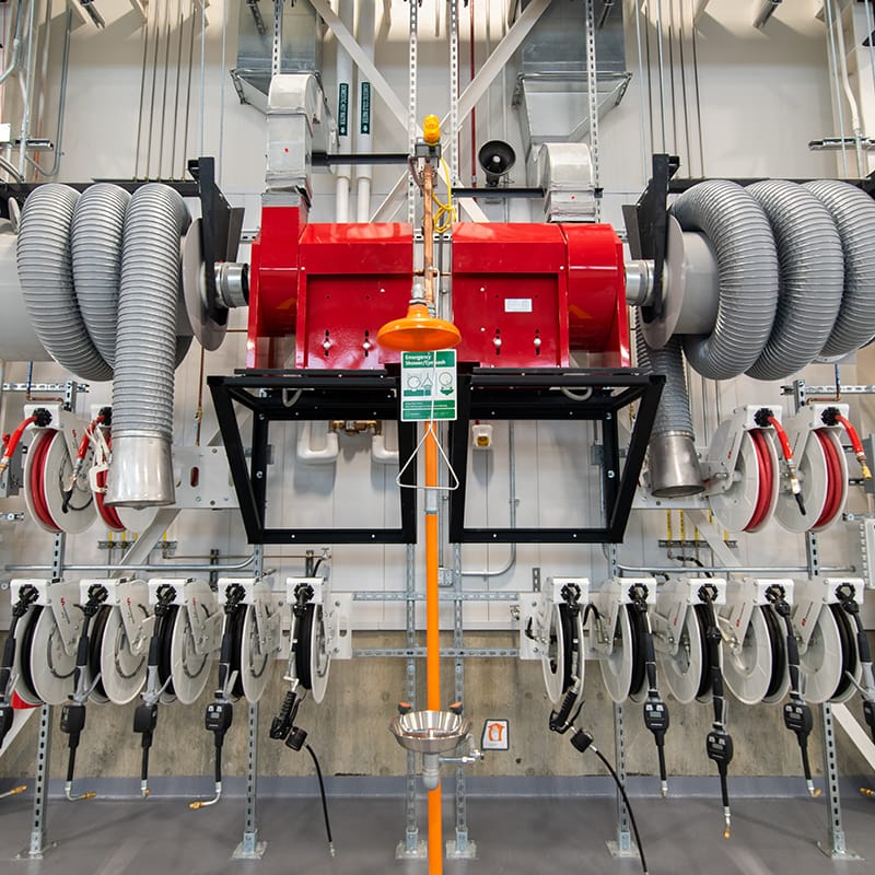 Vehicle maintenance equipment, exhaust extraction system and emergency eyewash station placed on a white wall of a garage.
