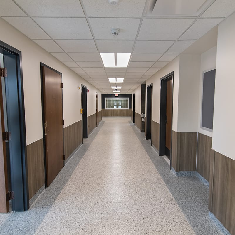 Hallway with numerous wooden doors, gray flooring, and white ceiling tiles located in the New York Army National Guard's new maintenance facility.