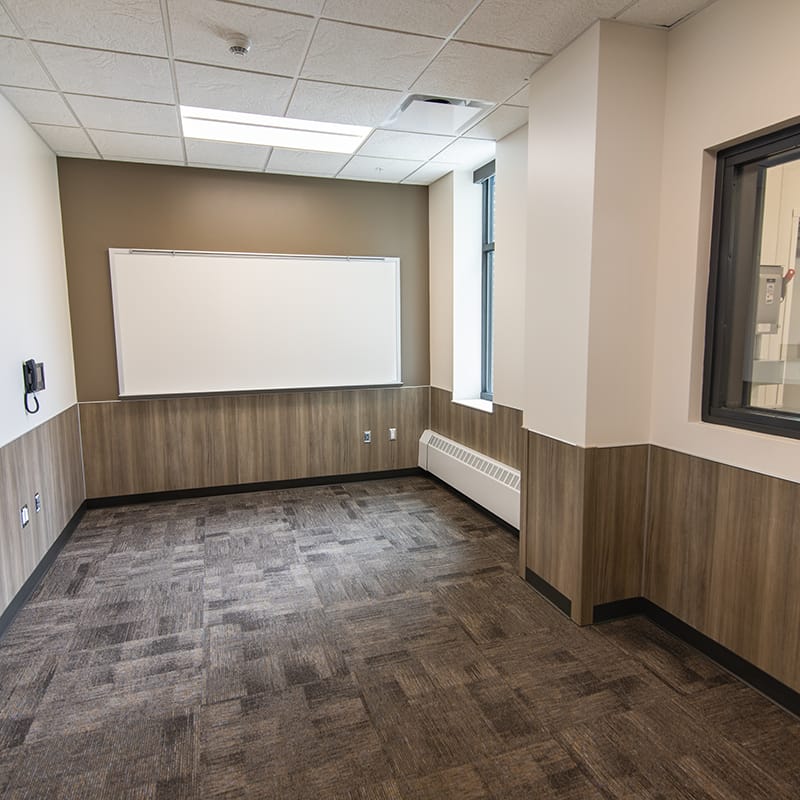 Meeting room with brown carpet, white walls, a whiteboard, telephone, and windows located in the New York Army National Guard's new maintenance facility.