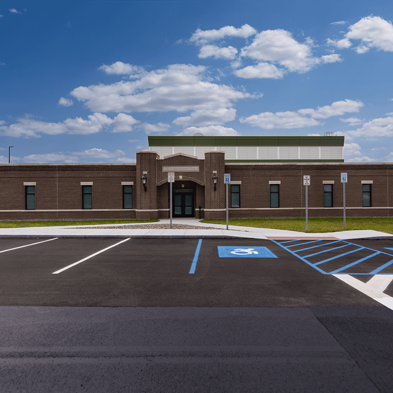 Brick and concrete facade with an asphalt paved parking lot, sidewalks, grass, and stone landscaping.